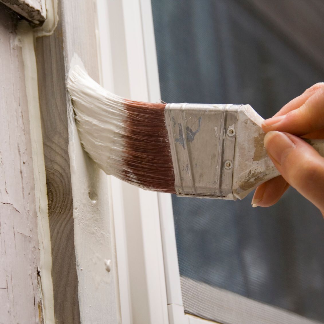 Mit einem Pinsel weiße Farbe auf einen Fensterrahmen auftragen.