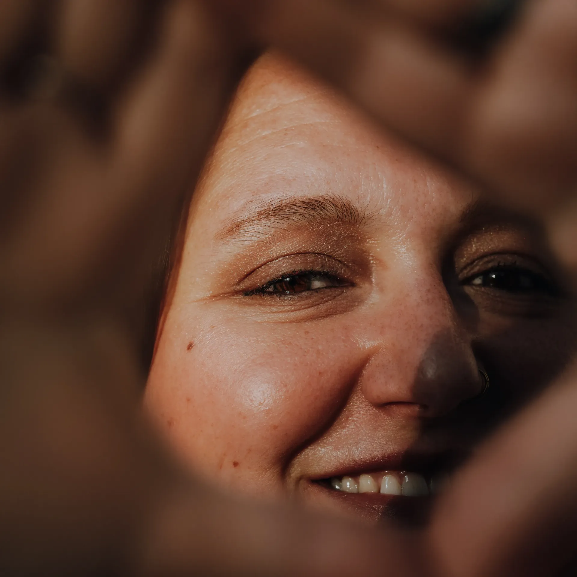 Frau hält beide Hände vor ihr Gesicht. Durch die Rautenförmige Öffnung ist ihr Auge zu sehen