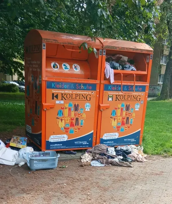 Altkleidercontainer in Duisburg-Hamborn mit vielen Kleidungsstücken und Abfällen davor