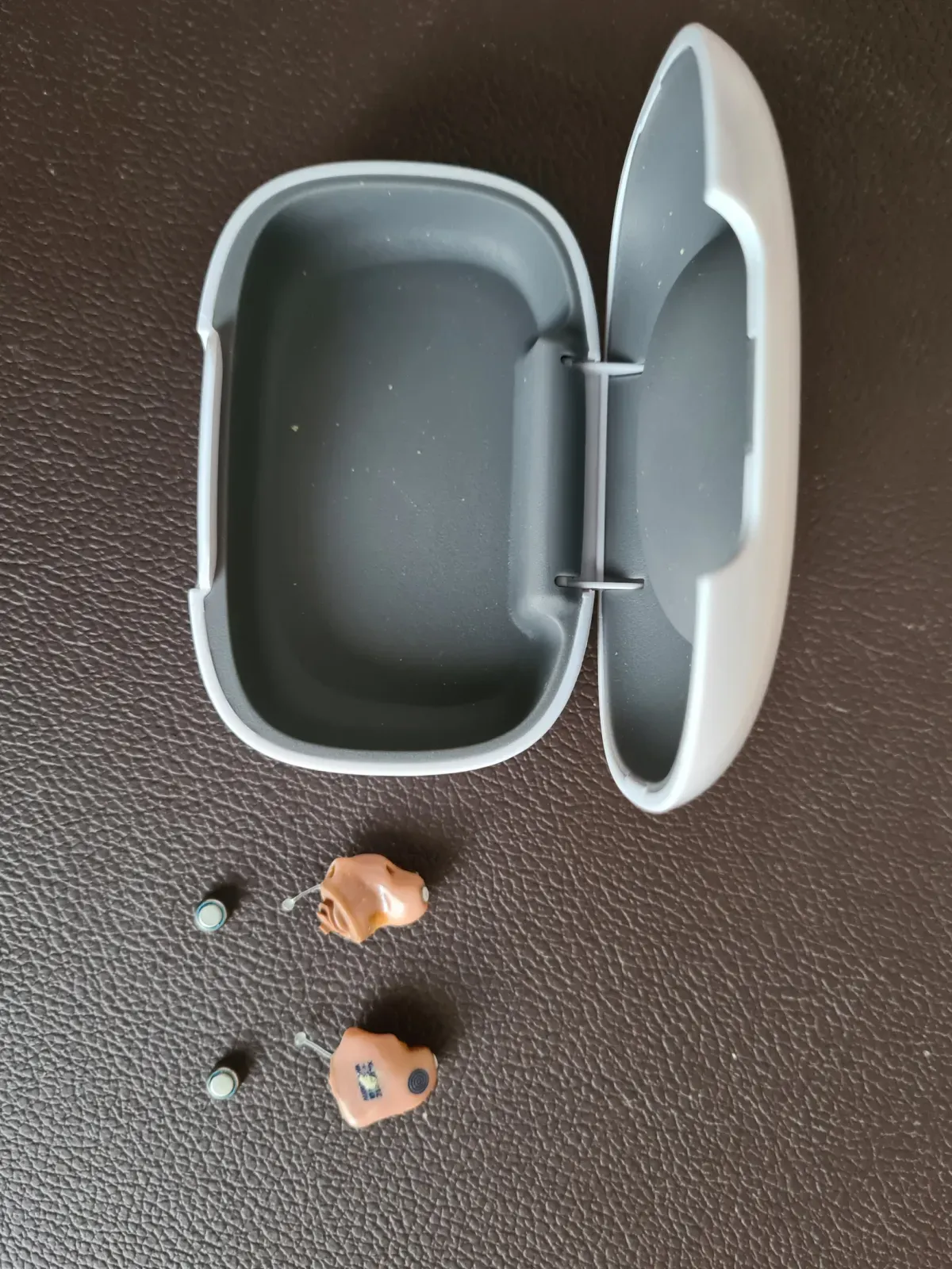 Kleines Hörhilfe Hörgerät mit Aufbewahrung Schale Hörer liegen daneben.