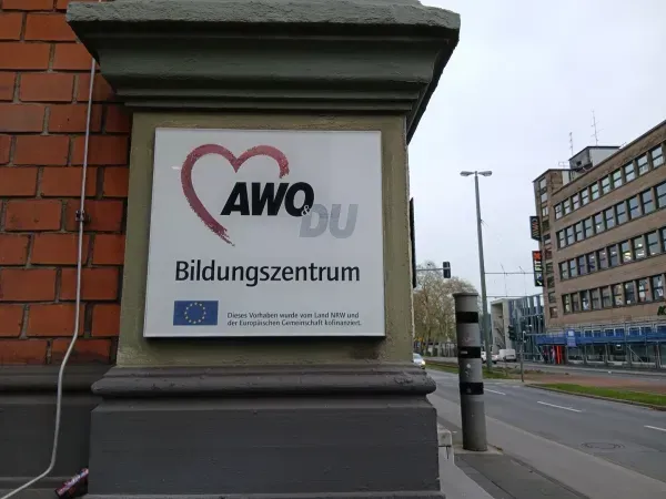 Schild vom AWD Bildungszentrum in Duisburg-Hamborn an einer Straße mit Gebäuden im Hintergrund