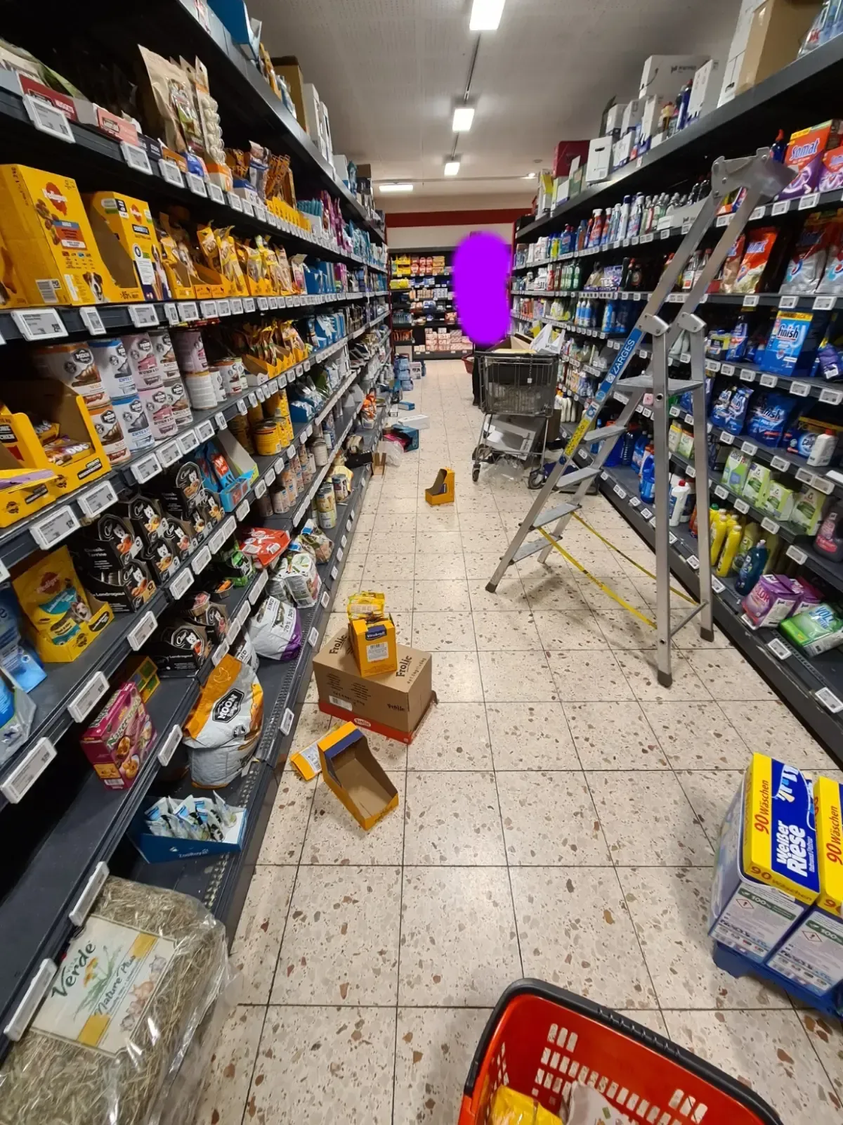 Kunde steht im REWE Duisburg in einem Gang mit Kartons und Ware auf dem Boden