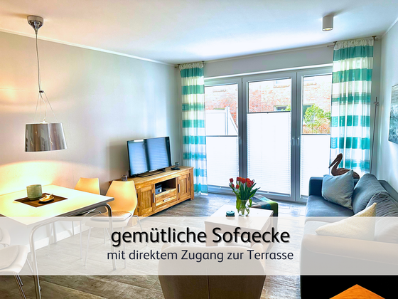 Wohnzimmer der FeWo StrandART in Norddeich mit Blick auf das gemütliche Sofaecke samt TV und Zugang zur Sonnenterrasse