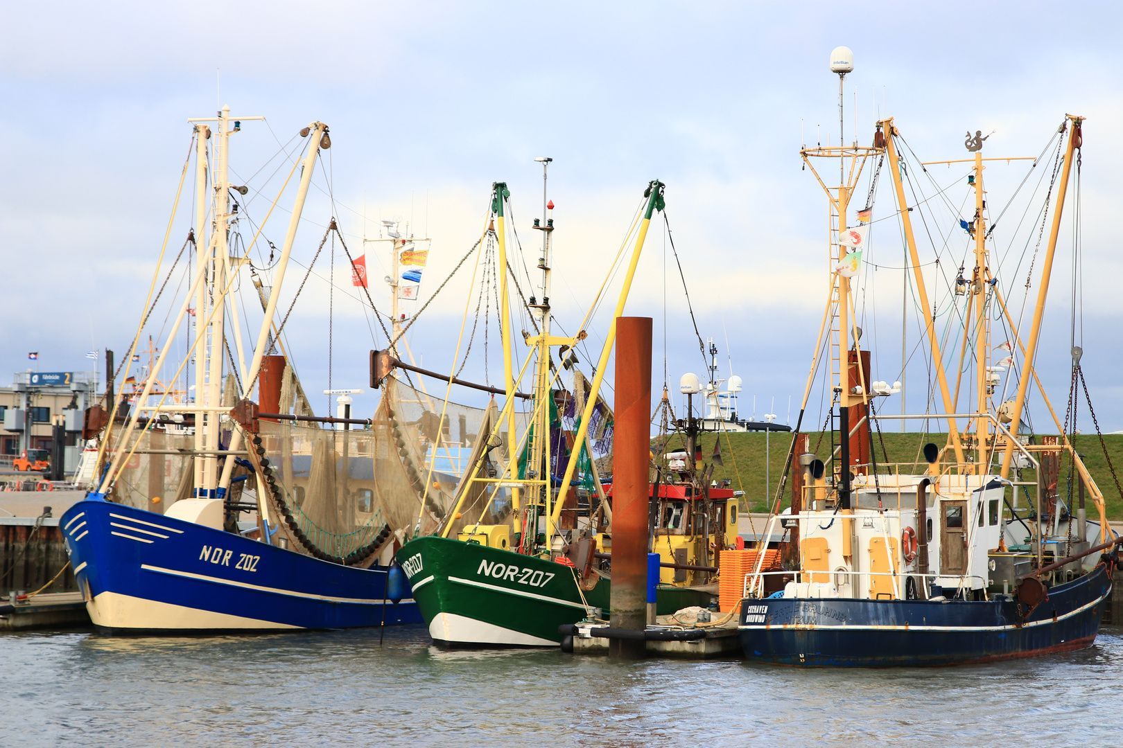 der verschlafene Fischerhafen. es sind 3 Fischkutter zu sehen, die im Hafen festgemacht haben. Zwei sind blau, der in der Mitte ist grün