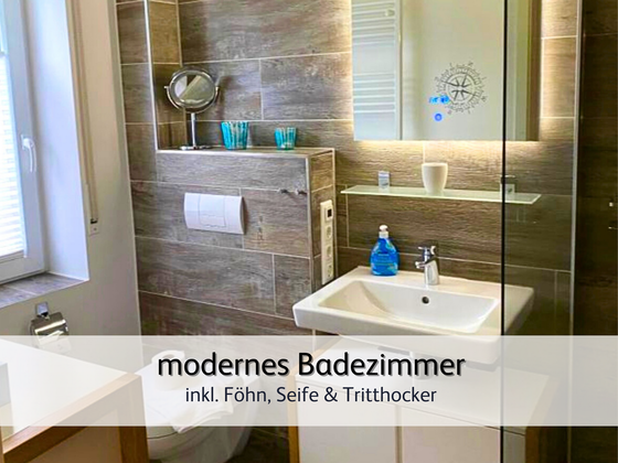 Badezimmer der Ferienwohnung StrandART in Norddeich in moderner Holzoptik und Fenster samt Spiegel, Schminkspiegel, Waschbecken und Seife