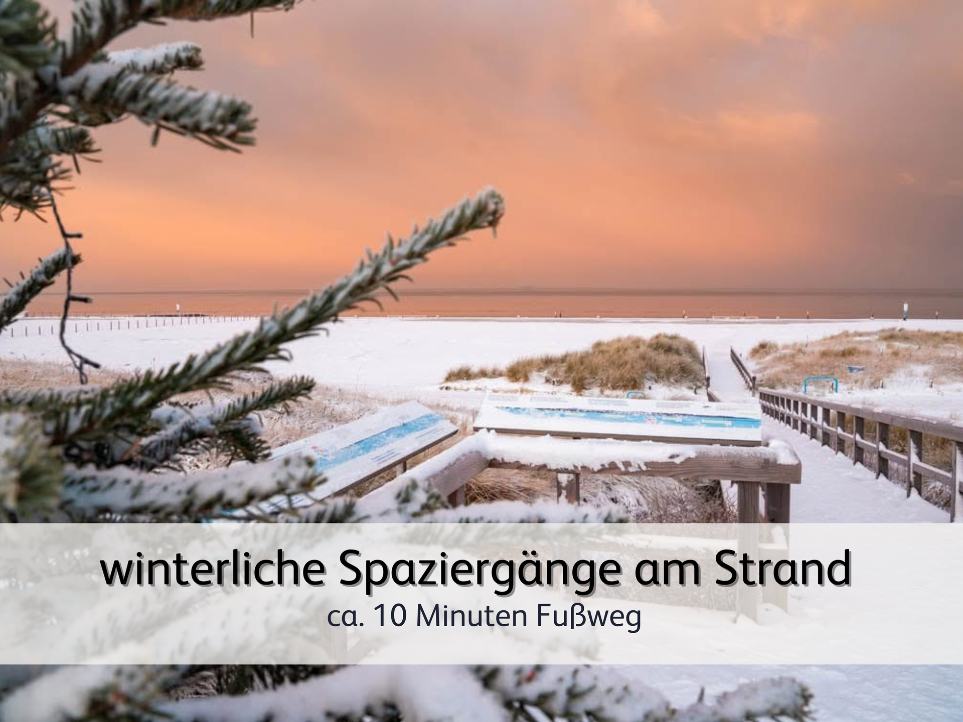 ein verschneiter Holzbohlenweg, der von den Dünen zum Strand in Norddeich führt. Auf der linken Seite steht ein verschneiter Tannenbam Der Strand und die Dünnen sind ebenfalls von Schnee bedeckt. Der Himmel im Hintergrund ist in ein weiches rot-orange gefärbt