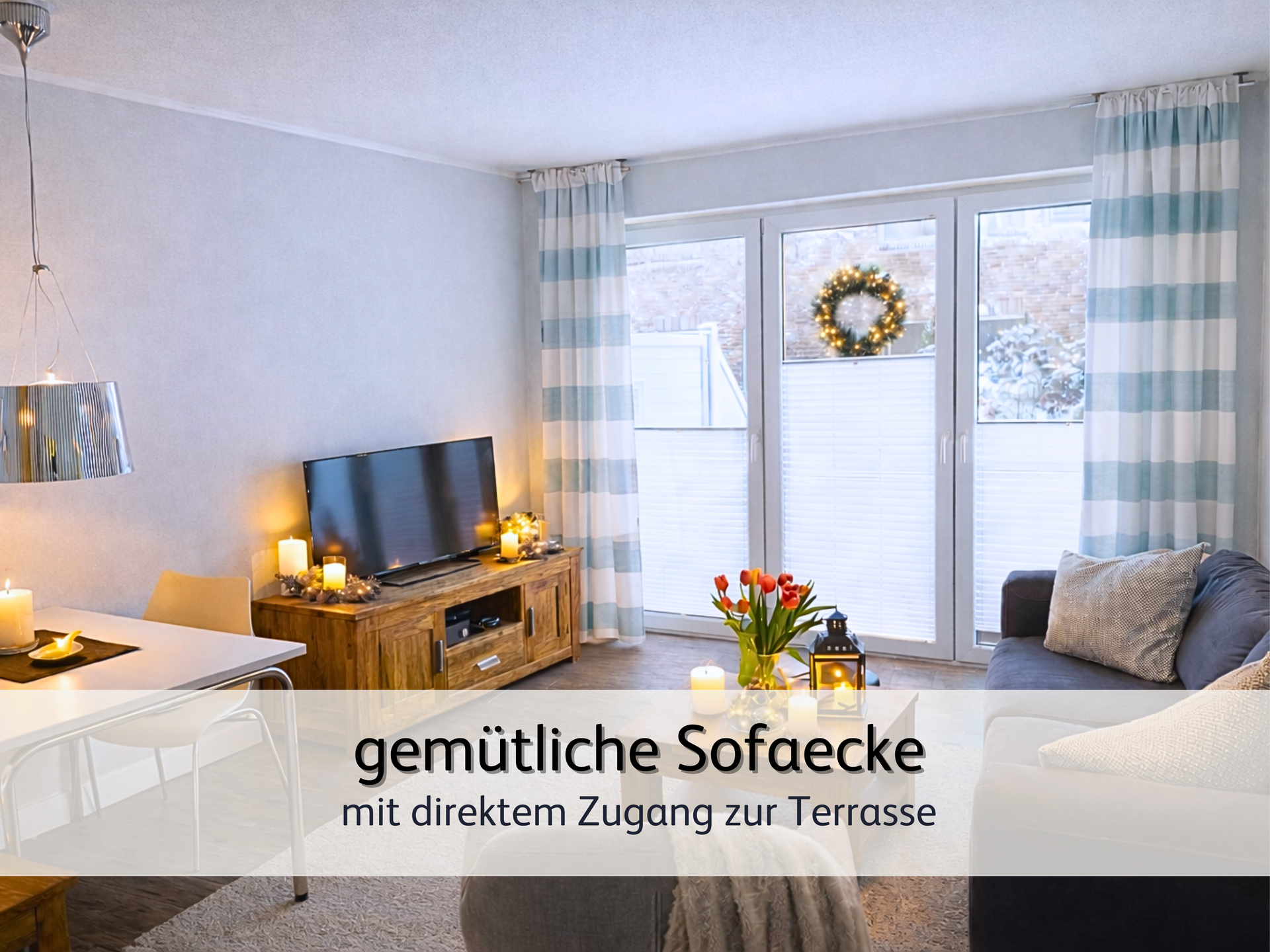 Wohnzimmer der FeWo StrandART in Norddeich mit Blick das Sideboard auf dem der Fernseher steht. Neben dem Fernseher stehen warm leuchtende Kerzen. Das Bild strahlt eine winterliche Wärme aus.