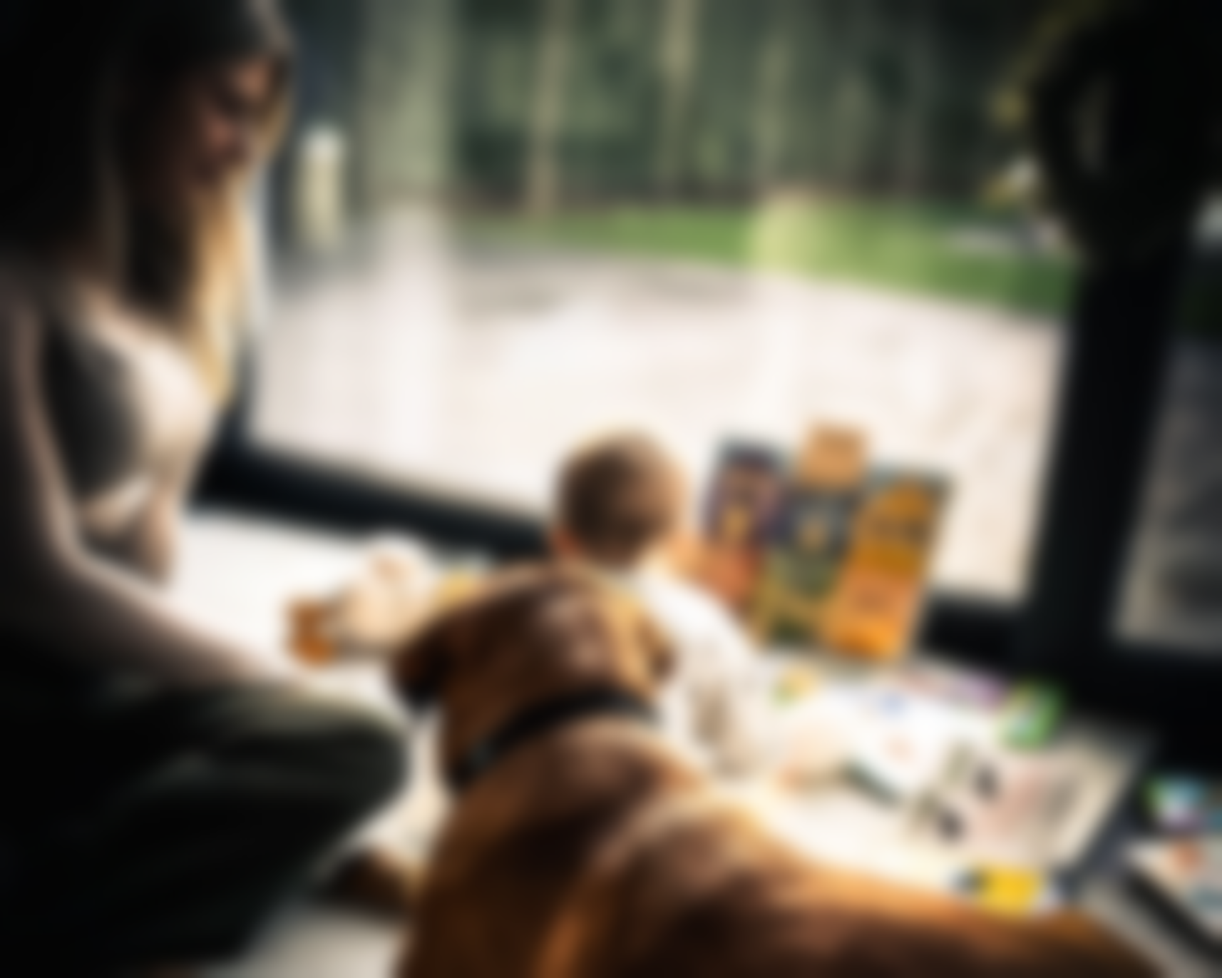 Frau und Baby schauen sich Bücher an, ein Hund liegt am Fenster.