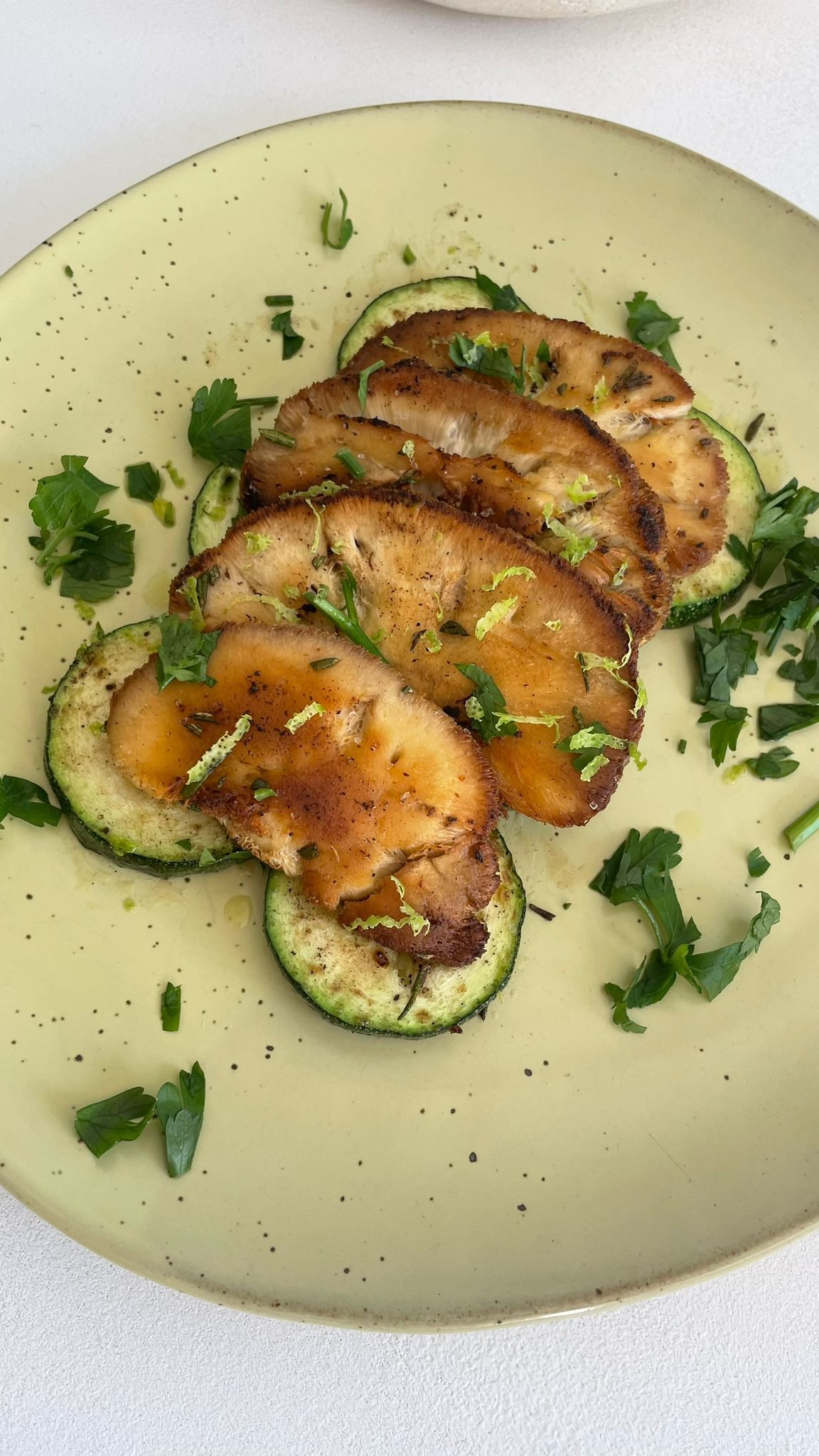 Gegrillter Igelstachelbart auf Zucchinischeiben, garniert mit Kräutern auf einem gelben Teller.