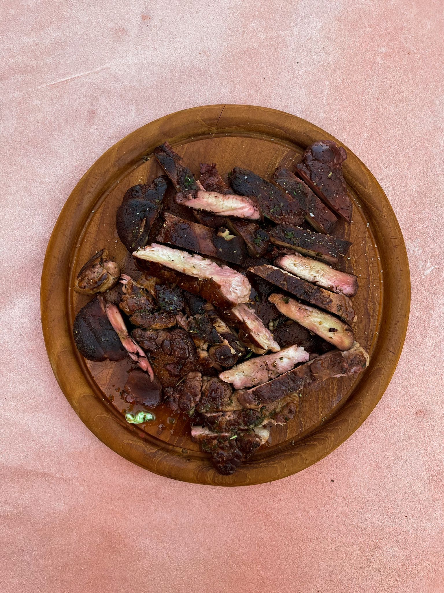 In Scheiben geschnittener, angebratener und geräucherter Igelstachelbart, angerichtet auf einem runden, strukturierten Holzbrett vor einem pfirsichfarbenen Hintergrund.