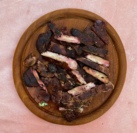 Gebratenes Steak aus dem Pilz Igelstachelbart in Scheiben auf einer Holzplatte, auf einer rosa Oberfläche angerichtet.