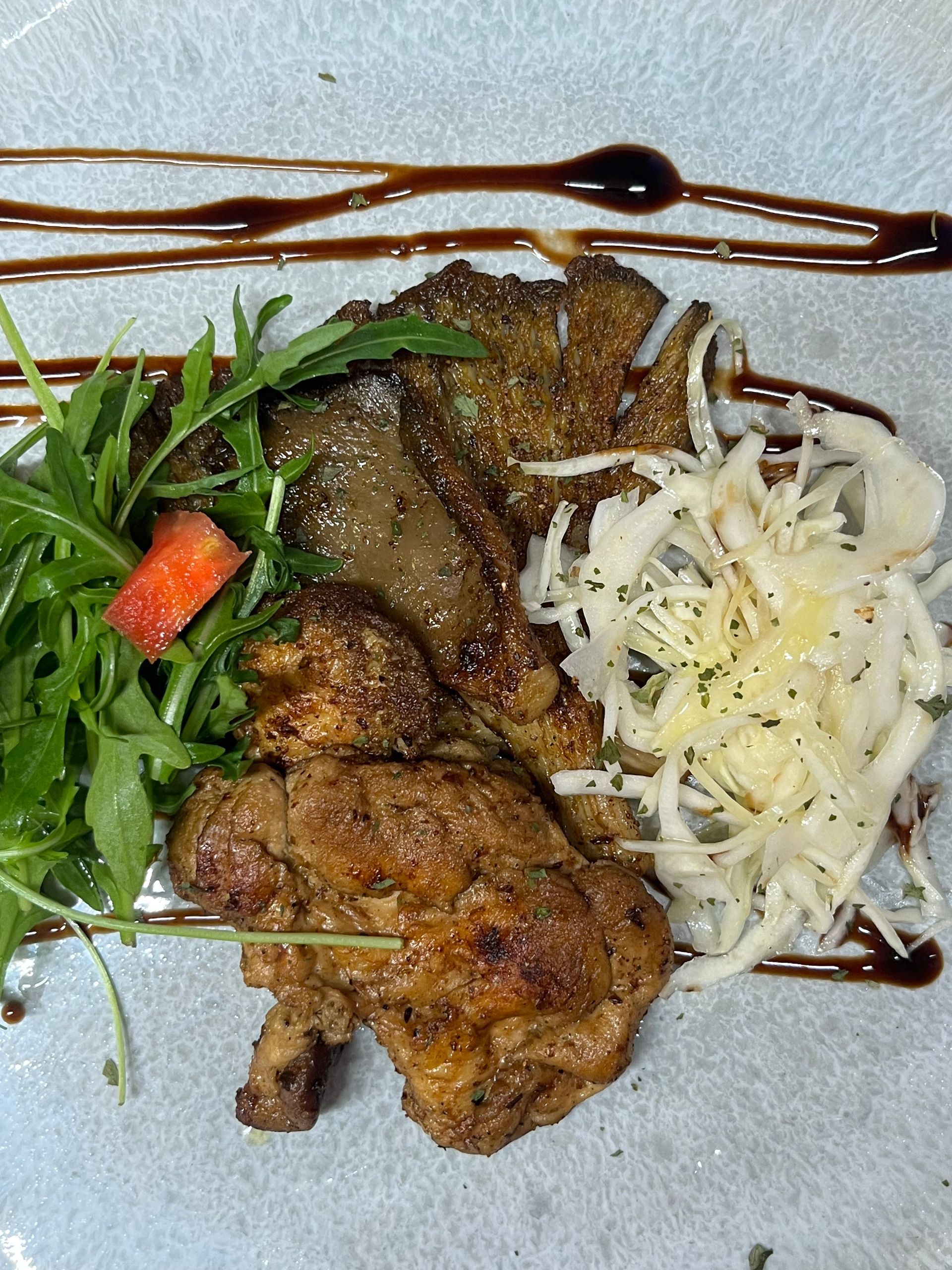 Teller mit gegrilltem Igelstachelbart mit Rucola, geschnittenem Kohl und Balsamico-Glasur auf einem blauen Teller.