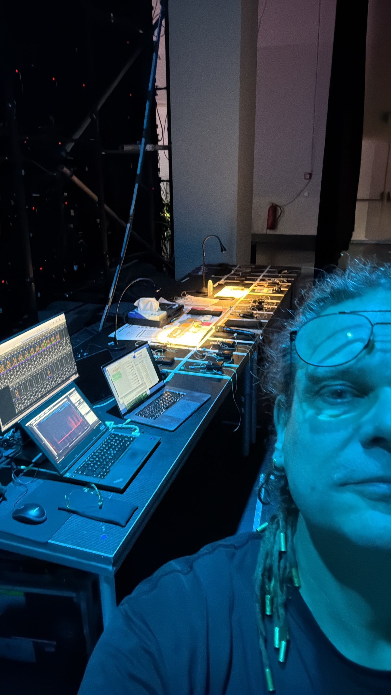 Eine Person steht in einem dunklen Raum vor einem langen, mit Technik vollgestopften Tisch. Blaues Licht erhellt die Szene.