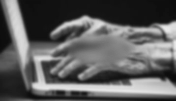 Die Hände eines alten Mannes tippen auf einer Laptop-Tastatur. Die Hände sind unscharf, um meine Makula-Degeneration zu veranschaulichen.