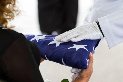 A hand in a white glove touching a folded American flag