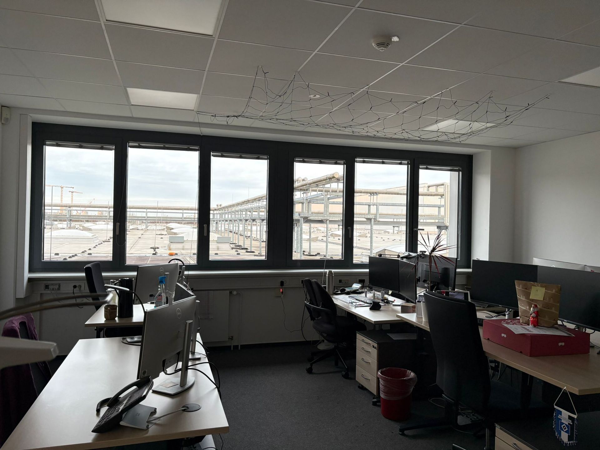 Bürointerieur mit Schreibtischen und Computern. Großes Fenster mit Blick auf eine Industriebaustelle.