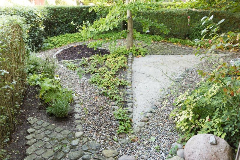 Gartenweg mit Natursteinen, Sand und Pflanzen in ruhiger Umgebung.