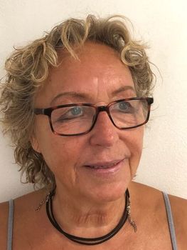 Lächelnde Frau mit kurzen grauen Haaren und Brille, die drinnen eine schwarze Halskette trägt