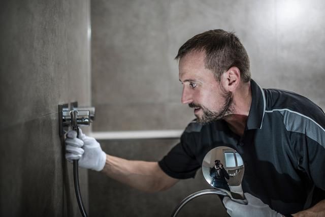 Ein Fachmann mit Handschuhen montiert eine moderne Duscharmatur an einer gefliesten Badezimmerwand.
