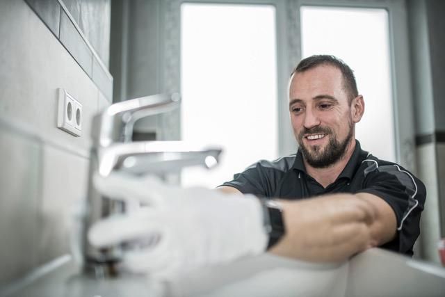 Eine Person mit weißen Handschuhen überprüft einen modernen Wasserhahn in einem gefliesten Badezimmer.