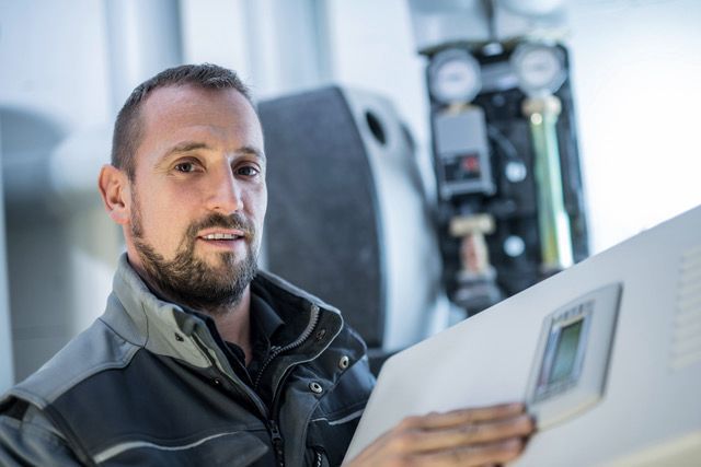 Eine Person in einer grauen Arbeitsjacke justiert das digitale Bedienfeld einer Heizungsanlage.
