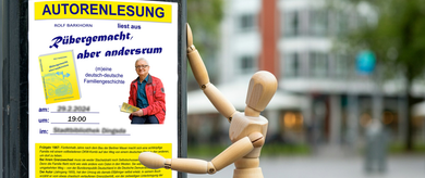Eine Holzpuppe klebt ein Plakat an, das Plakat kündigt eine Lesung an. Erstellt mit KI nach Idee von Rolf Barkhorn