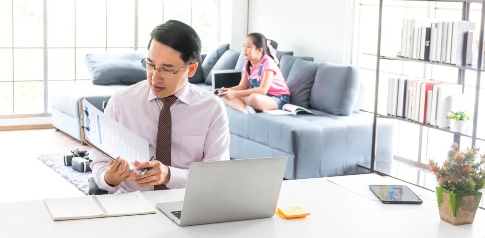 man working on computer with child on sofa behind