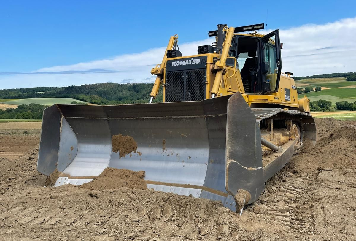 Ein gelber Bulldozer schiebt an einem sonnigen Tag Erde über ein Feld.