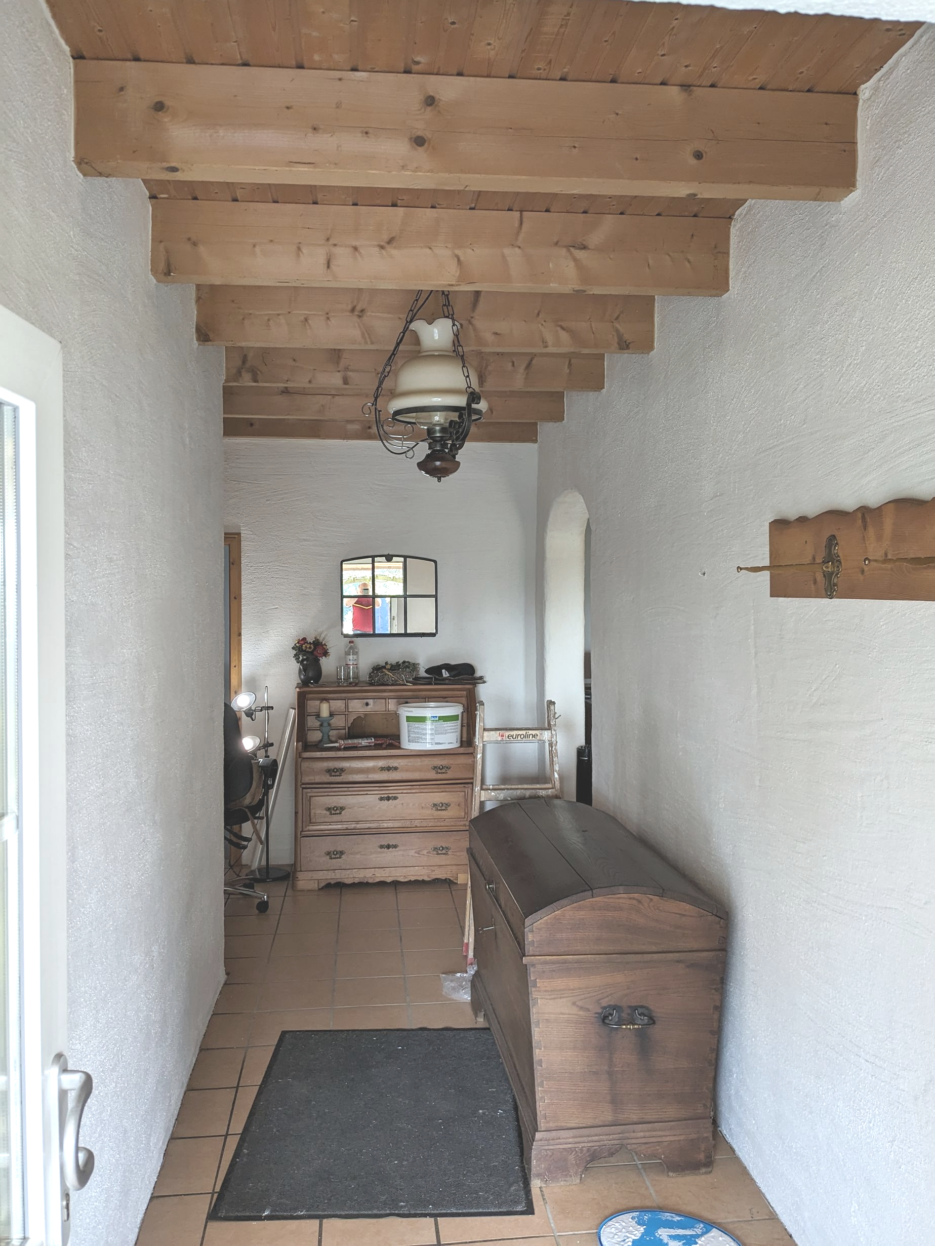 Flur mit strukturierten weißen Wänden, Holzbalken, einer Truhe und einem kleinen Tisch.