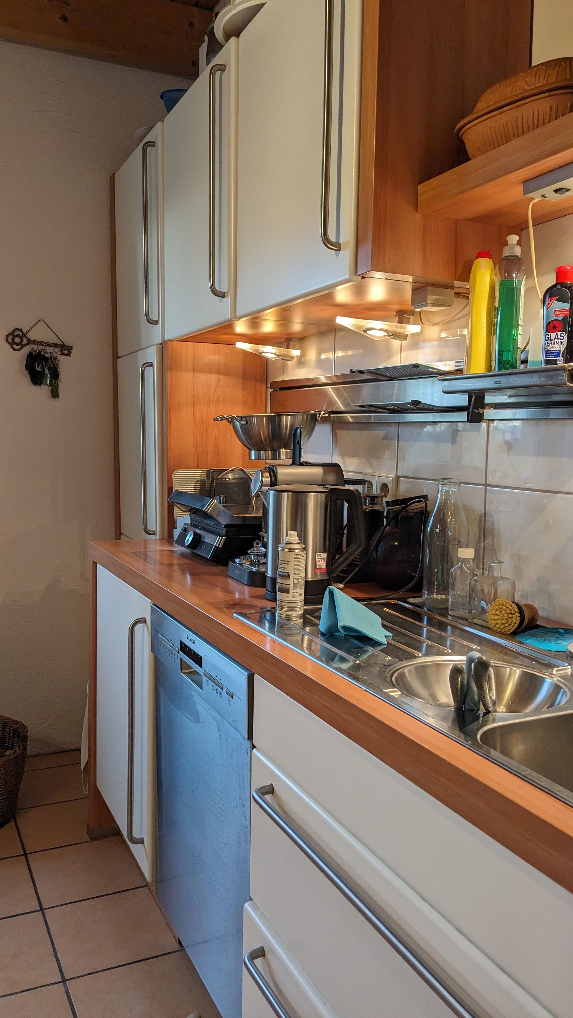 Küche mit weißen Schränken, Geräten aus Edelstahl, Holzarbeitsplatte und Fliesenboden.