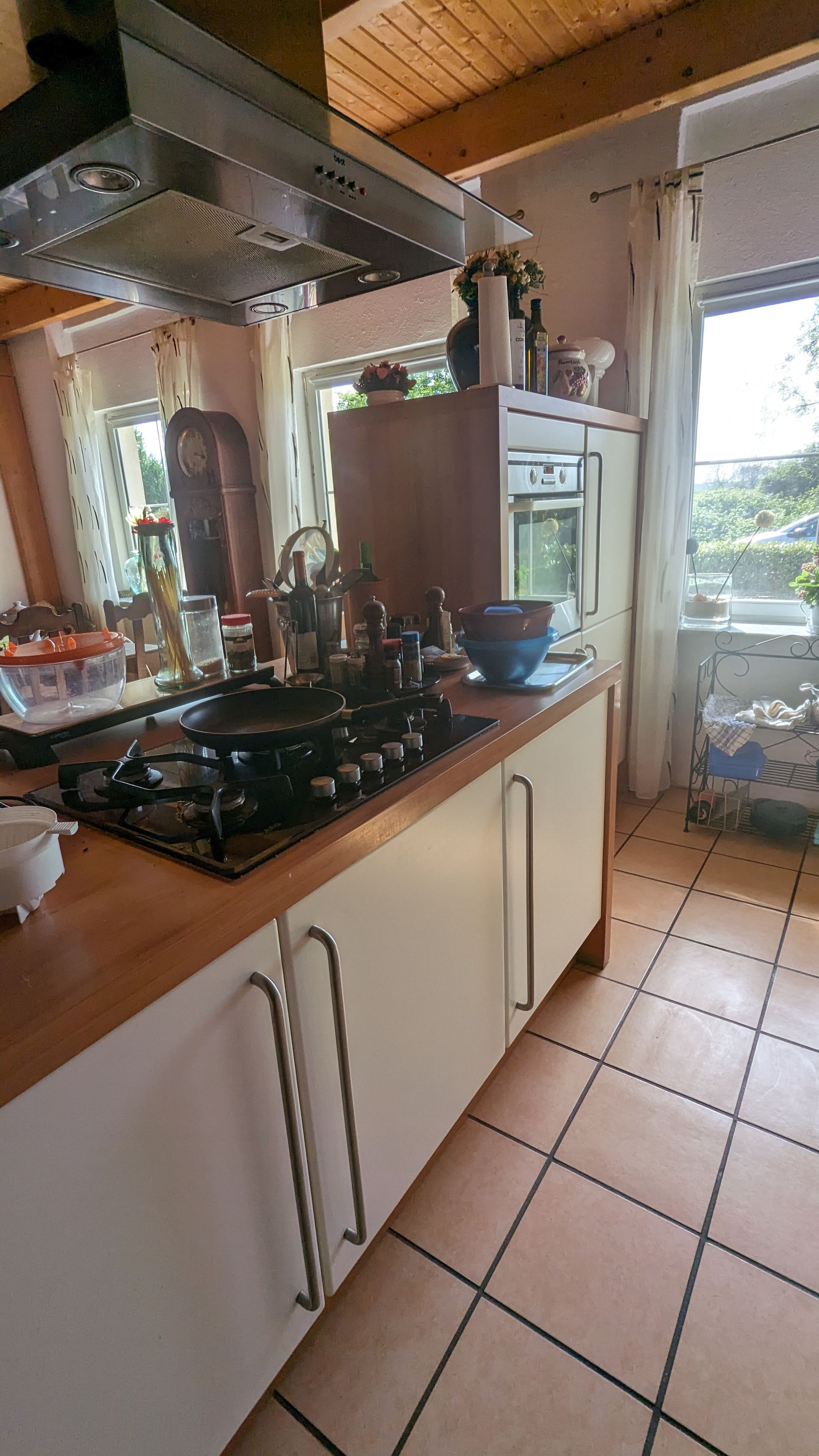 Küche mit weißen Schränken, Holzarbeitsplatte und Gasherd. Fliesenboden, Fenster mit Vorhängen.