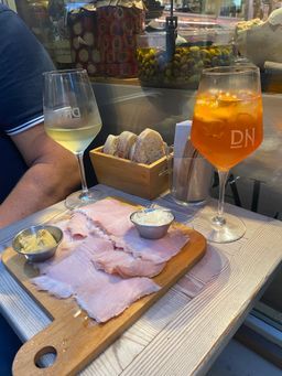 Wein und Orangensaft neben Wurstwaren auf einem Café-Tisch am Fenster