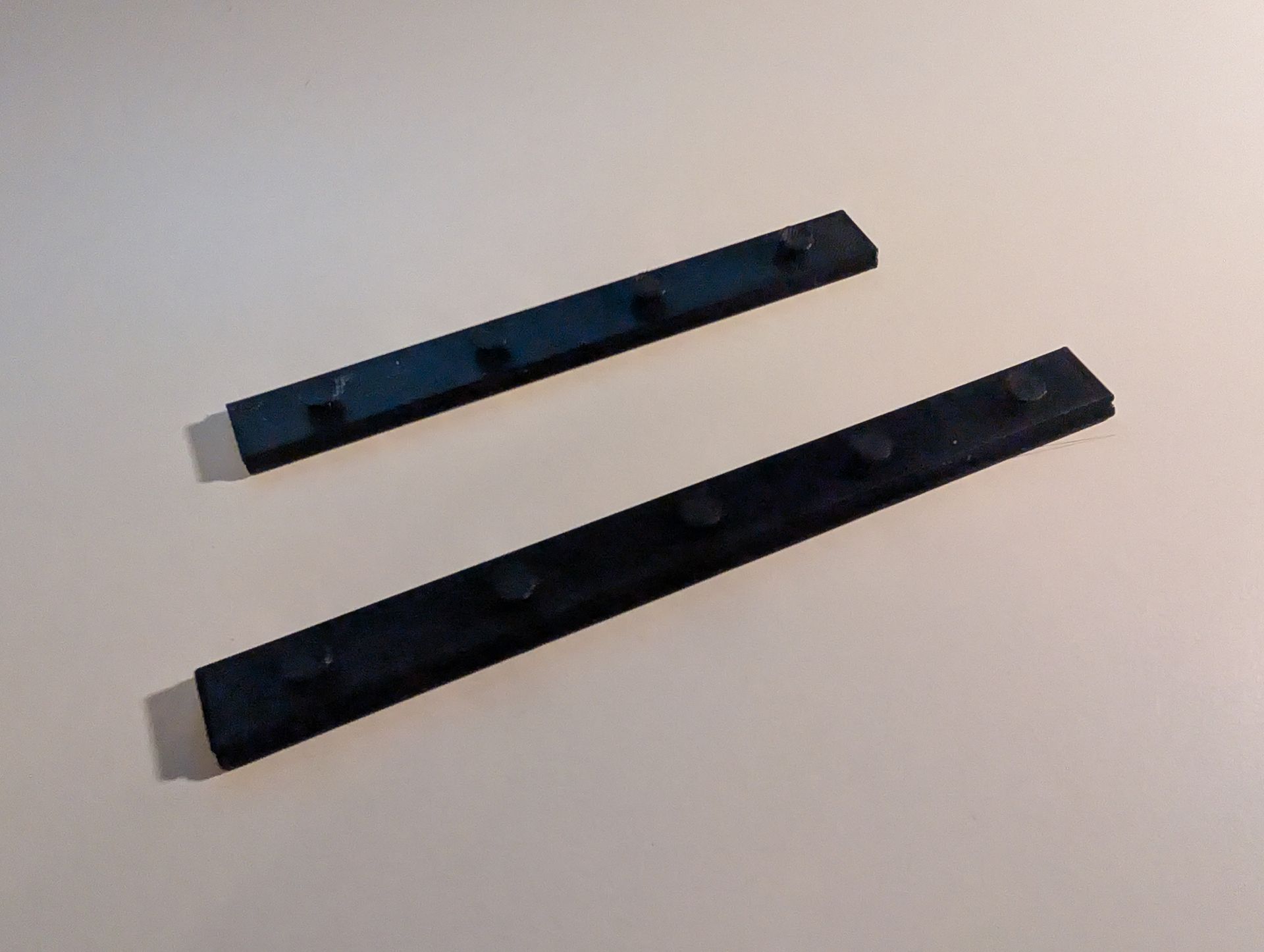 Schwarz-gelbes 3D-gedrucktes Werkzeug, wahrscheinlich für eine bestimmte Maschine oder ein bestimmtes Gerät, schräg auf einer weißen Oberfläche platziert.