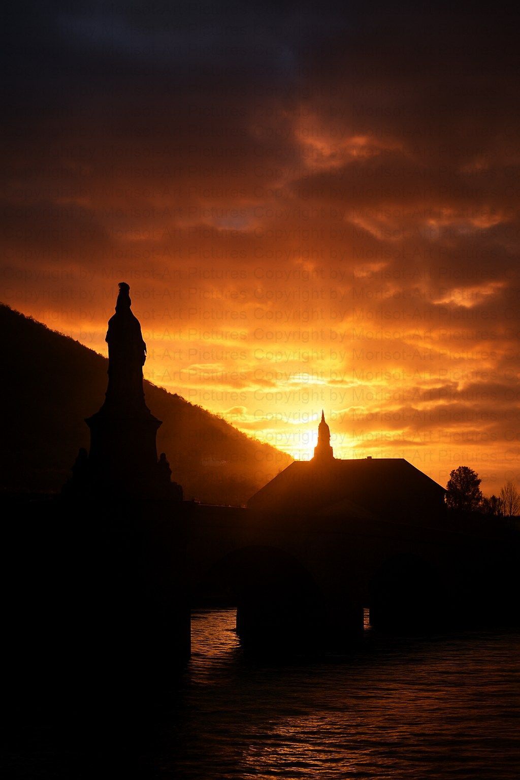 Silhouette von Brücke und Gebäuden vor einem feuerroten Sonnenuntergang über dem Wasser.