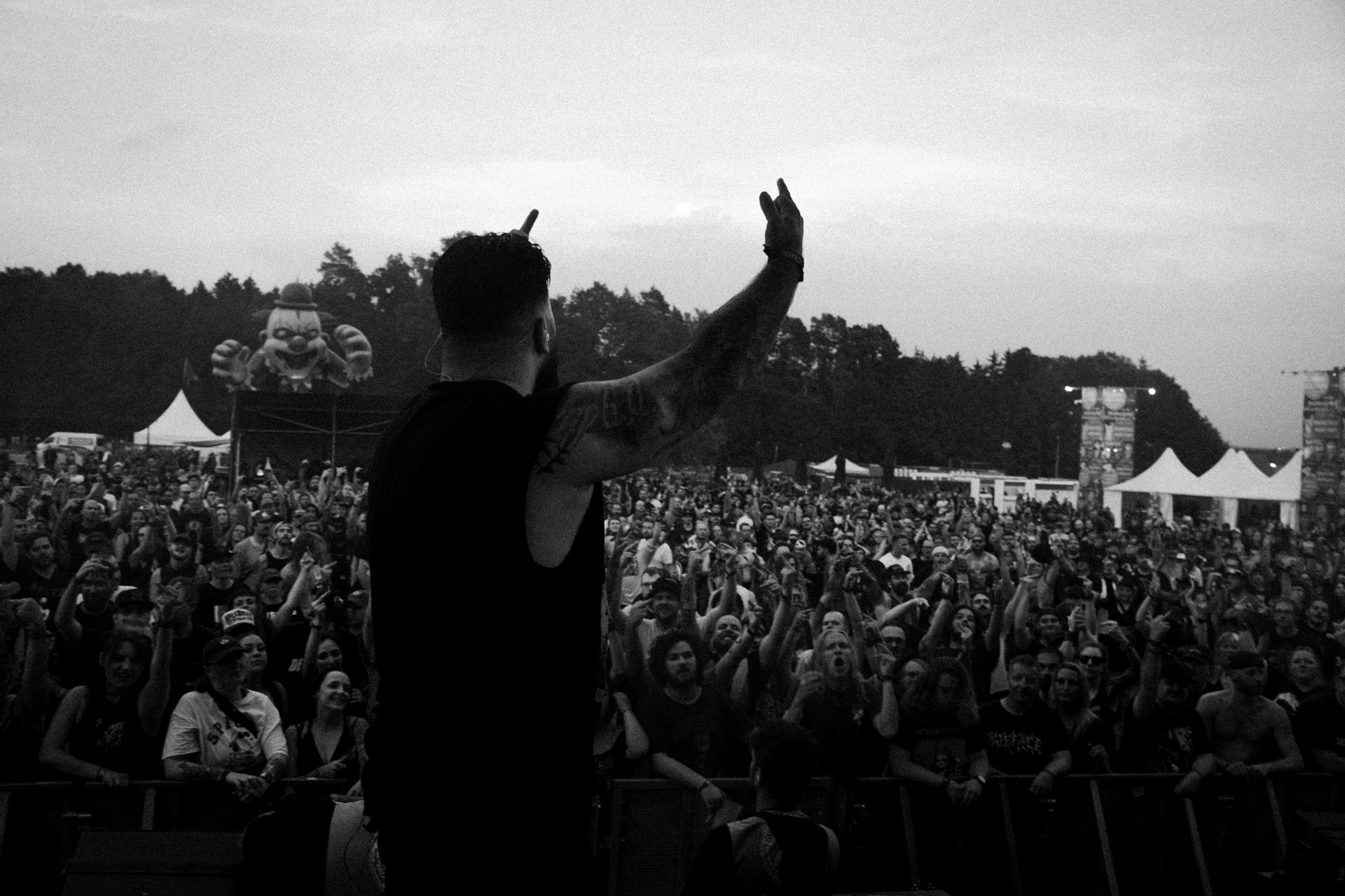 Musiker zeigt Mittelfinger auf Bühne vor Menschen auf einen Horror clown in der Ferne