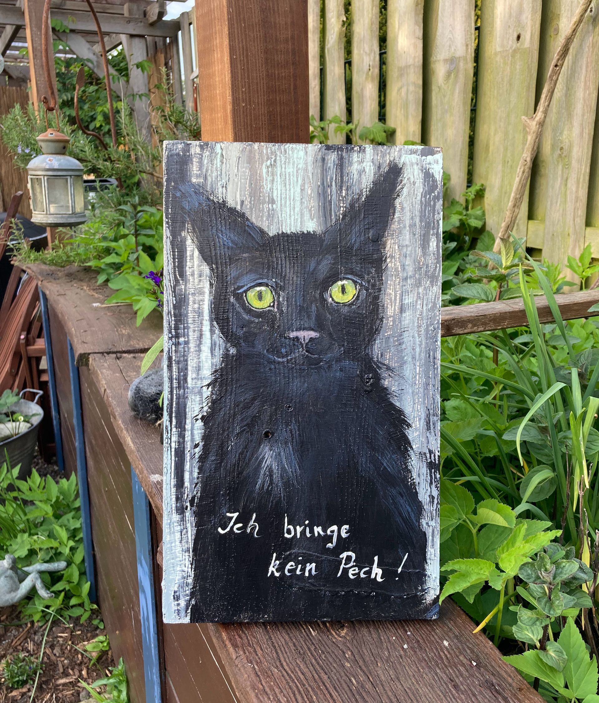 Eine schwarze Katze handgemalt auf Altholz mit der Aufschrift: 