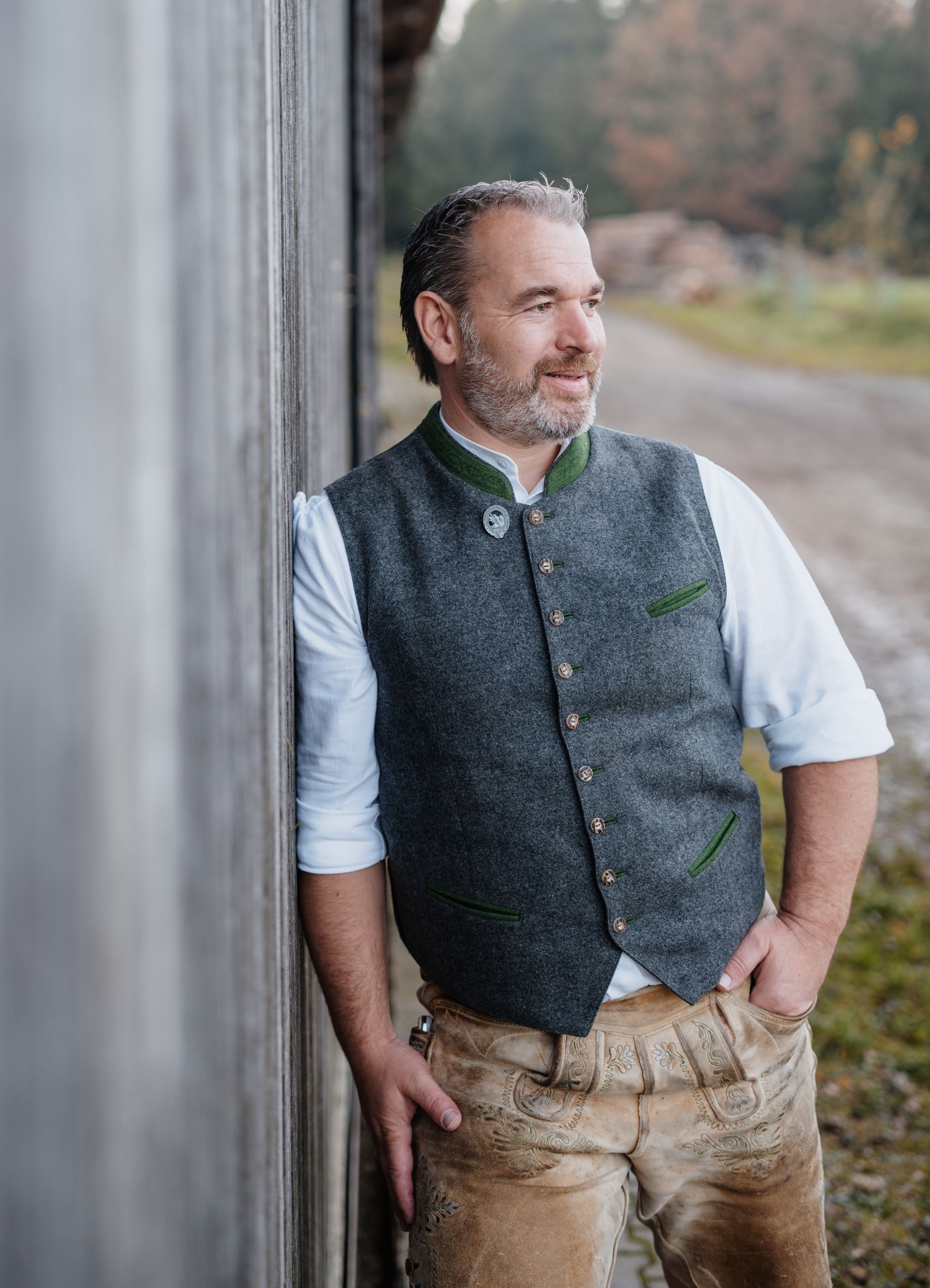 Matthias Plattner in traditioneller Weste und Hose lehnt an einer Holzkonstruktion und blickt aus dem Bild.