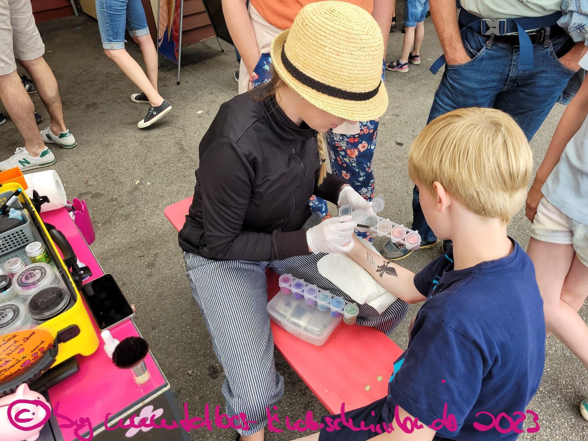 Eine Frau klebt einem Jungen bei einer Freiluftveranstaltung ein temporäres Tattoo auf den Arm.