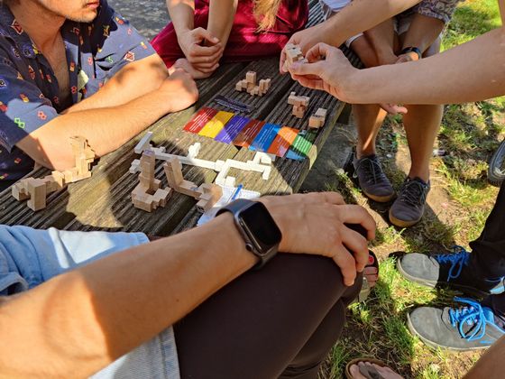 Menschen sitzen im Freien um Rätselelemente, halten diese in den Händen