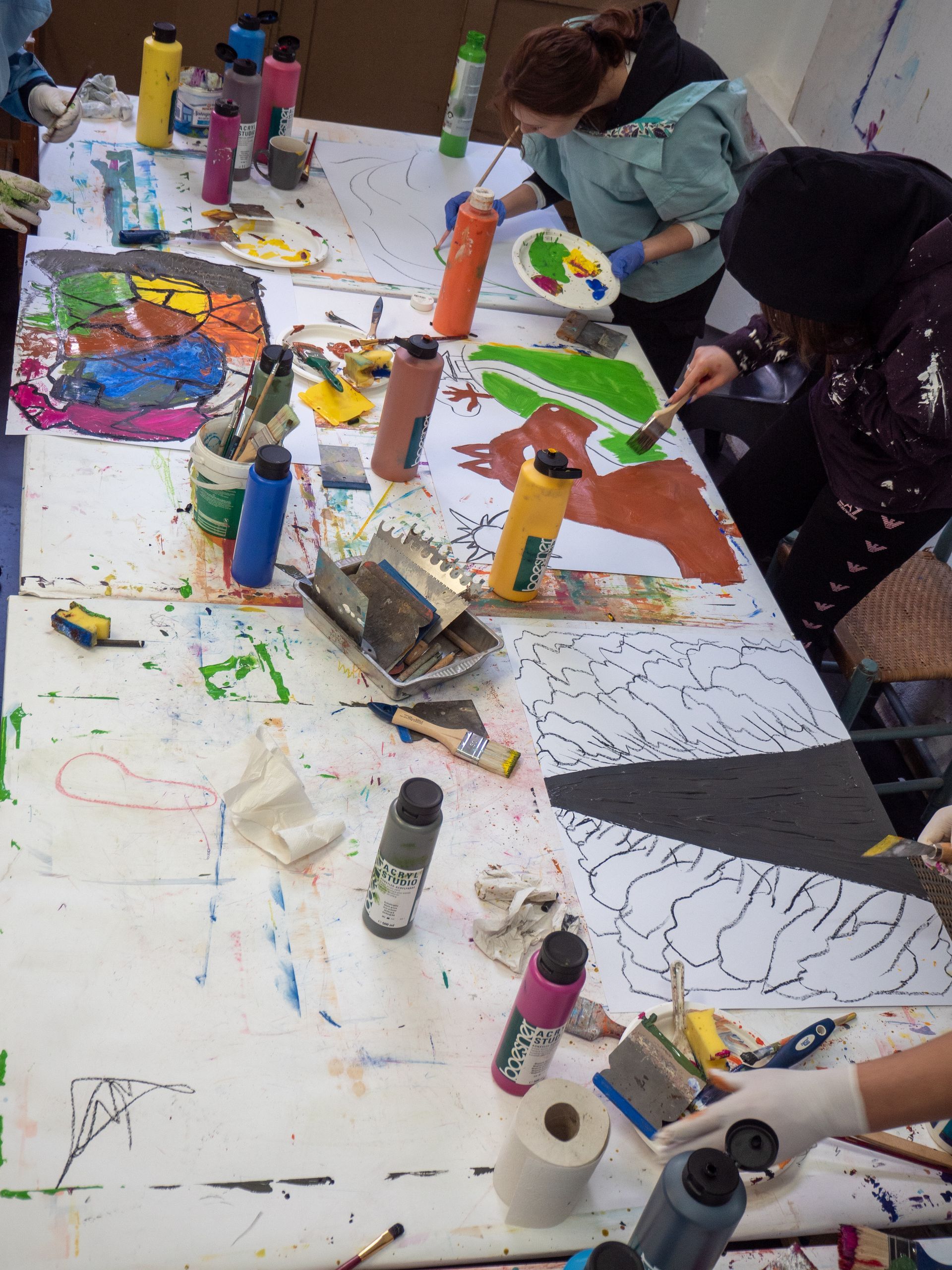 Jugendliche stehen an einem Tisch und malen mit Acrylfarben