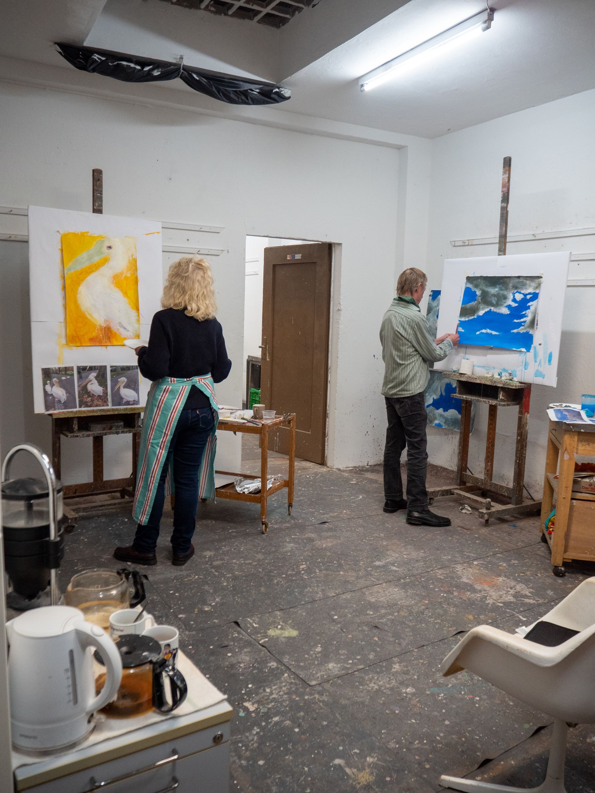 Eine Frau und ein Mann stehen in einem Atelier  jeweils vor einem Stativ und malen