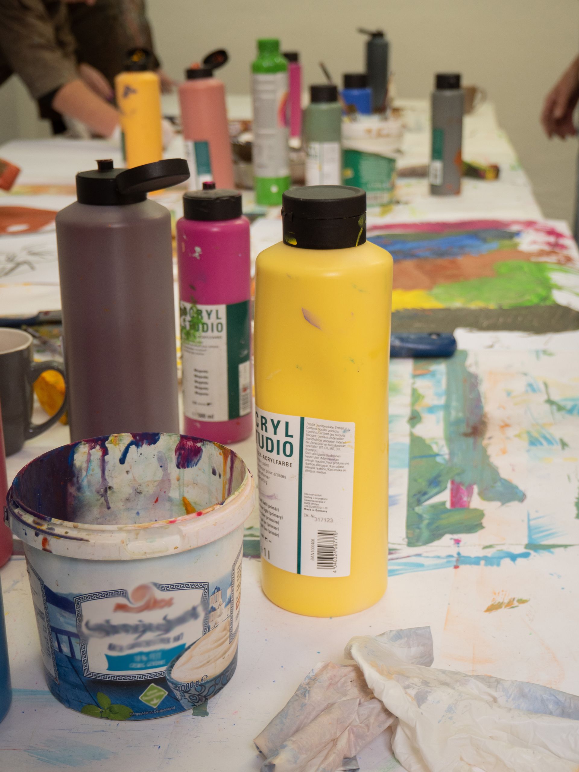 Tischsituation mit Acrylfarben, Bechern und Bildern