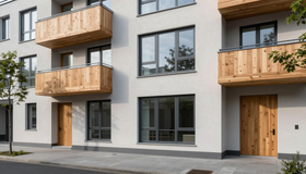 Modernes Mehrfamilienhaus mit Holzbalkonen, großen Fenstern und einer grauen Fassade entlang eines Gehwegs