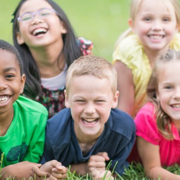 Fröhliche, lachende Kinder auf einer Wiese liegend