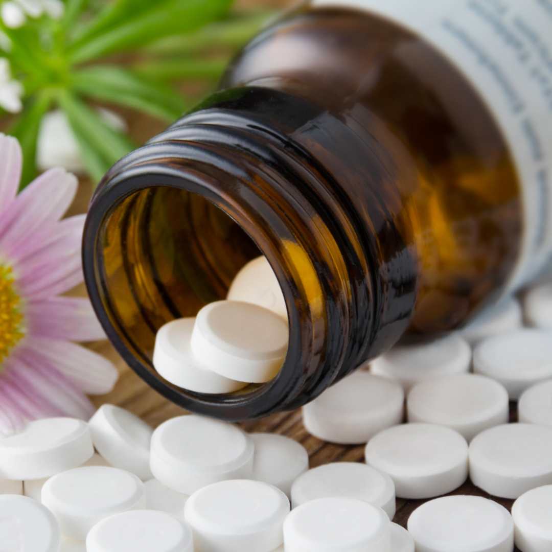 Nahaufnahme von mehreren Schüßler Salz Tabletten. Liegen vor einen Glasfläschchen auf dem Tisch mit einer Blume im Hintergrund