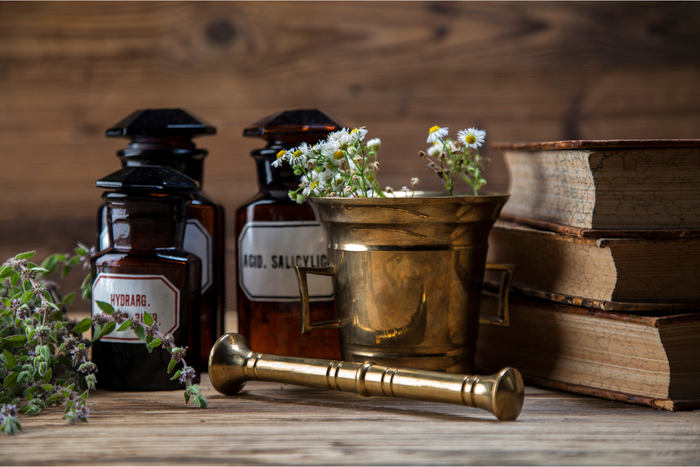 Gänseblümchen in einem goldenen Mörser, alten Büchern und drei Arzneibehältern aus Glas