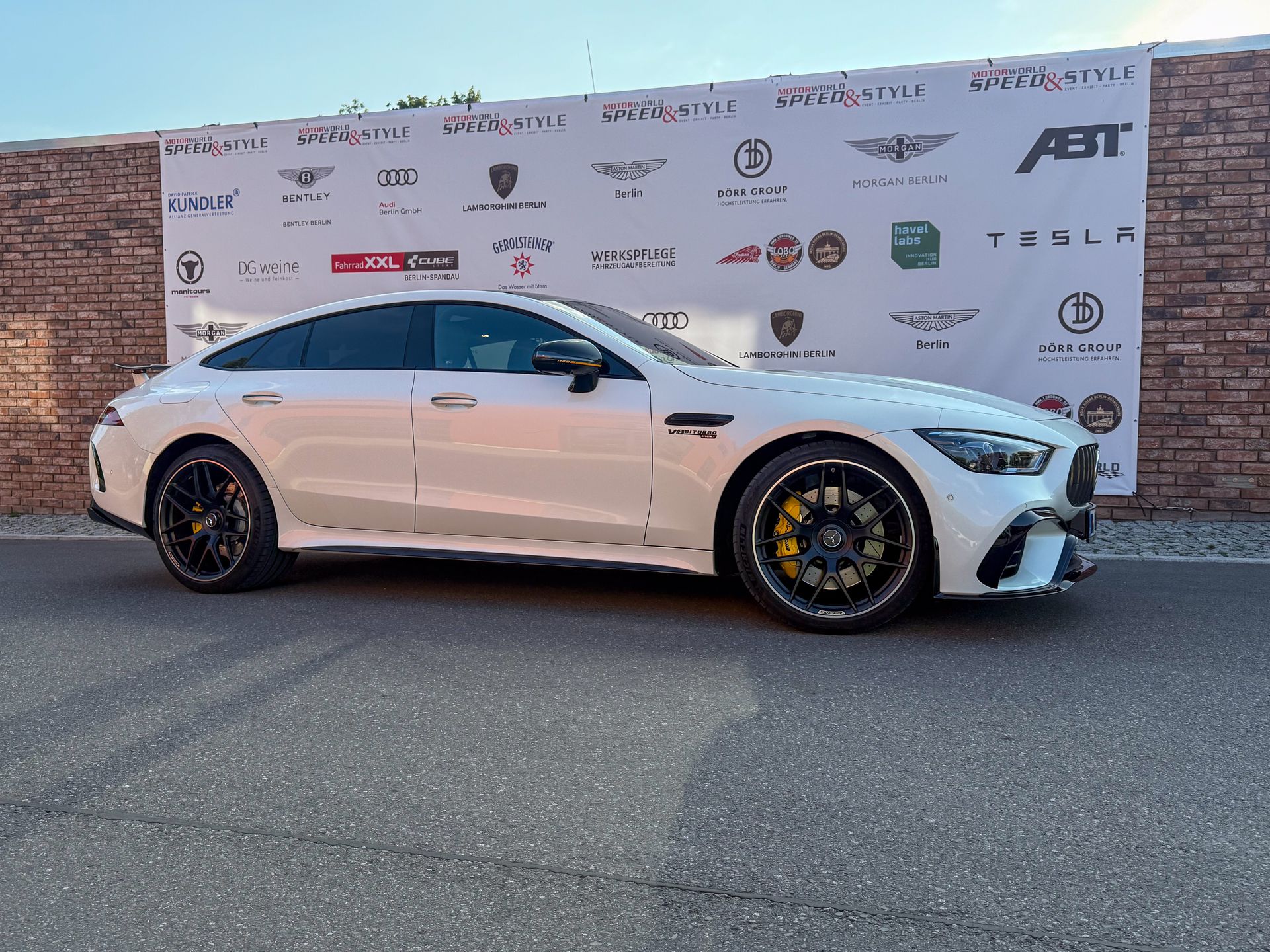 weißer AMG GT63s seitlich vor einer stein wand mit Werbung von Sportwagen Marken, Mercedes Benz AMG mieten Berlin 