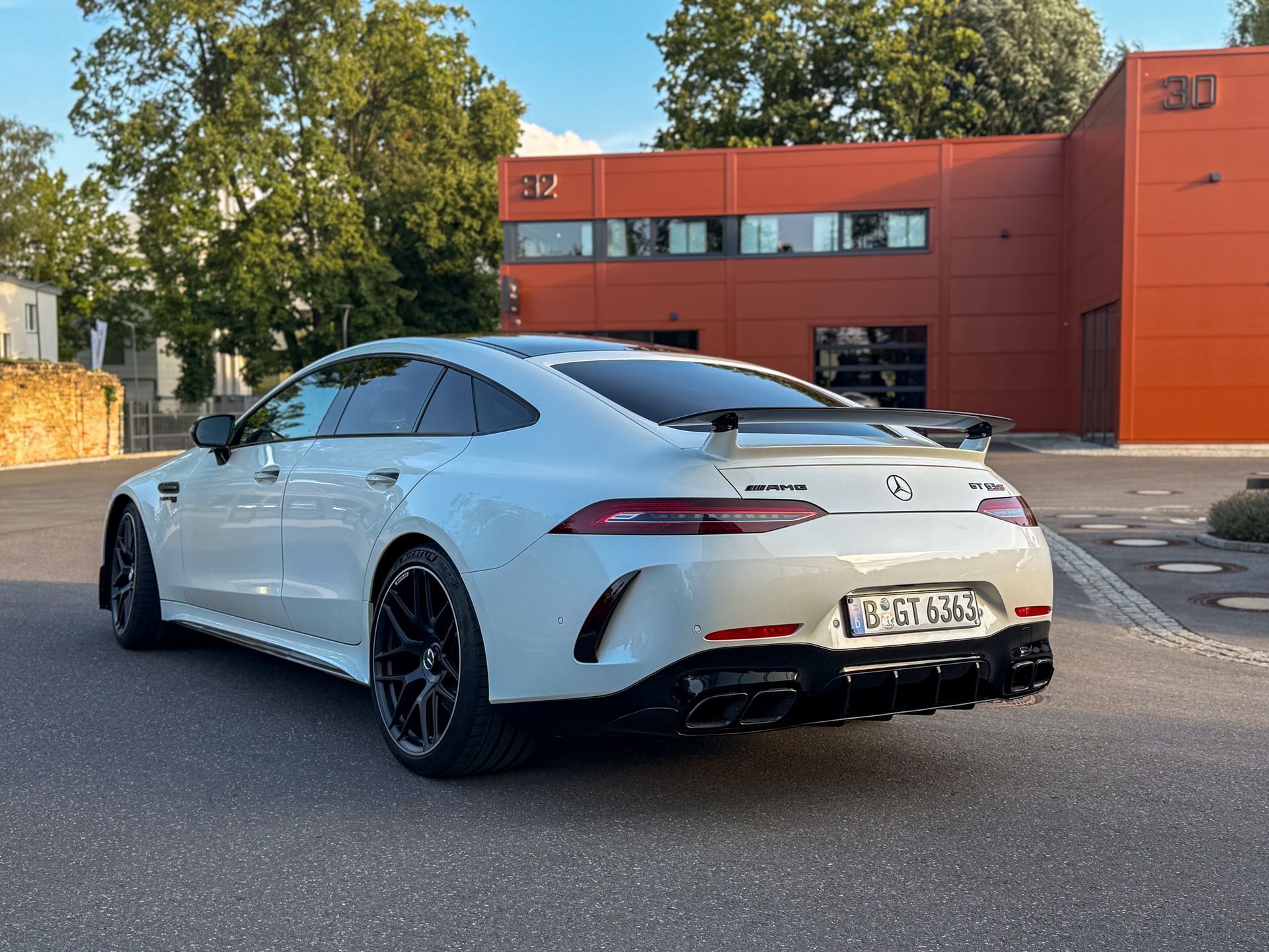 Weißer Mercedes-AMG GT63s 4-Türer von hinten links vor moderner Industriearchitektur in Berlin günstig AMG fahren in Berlin