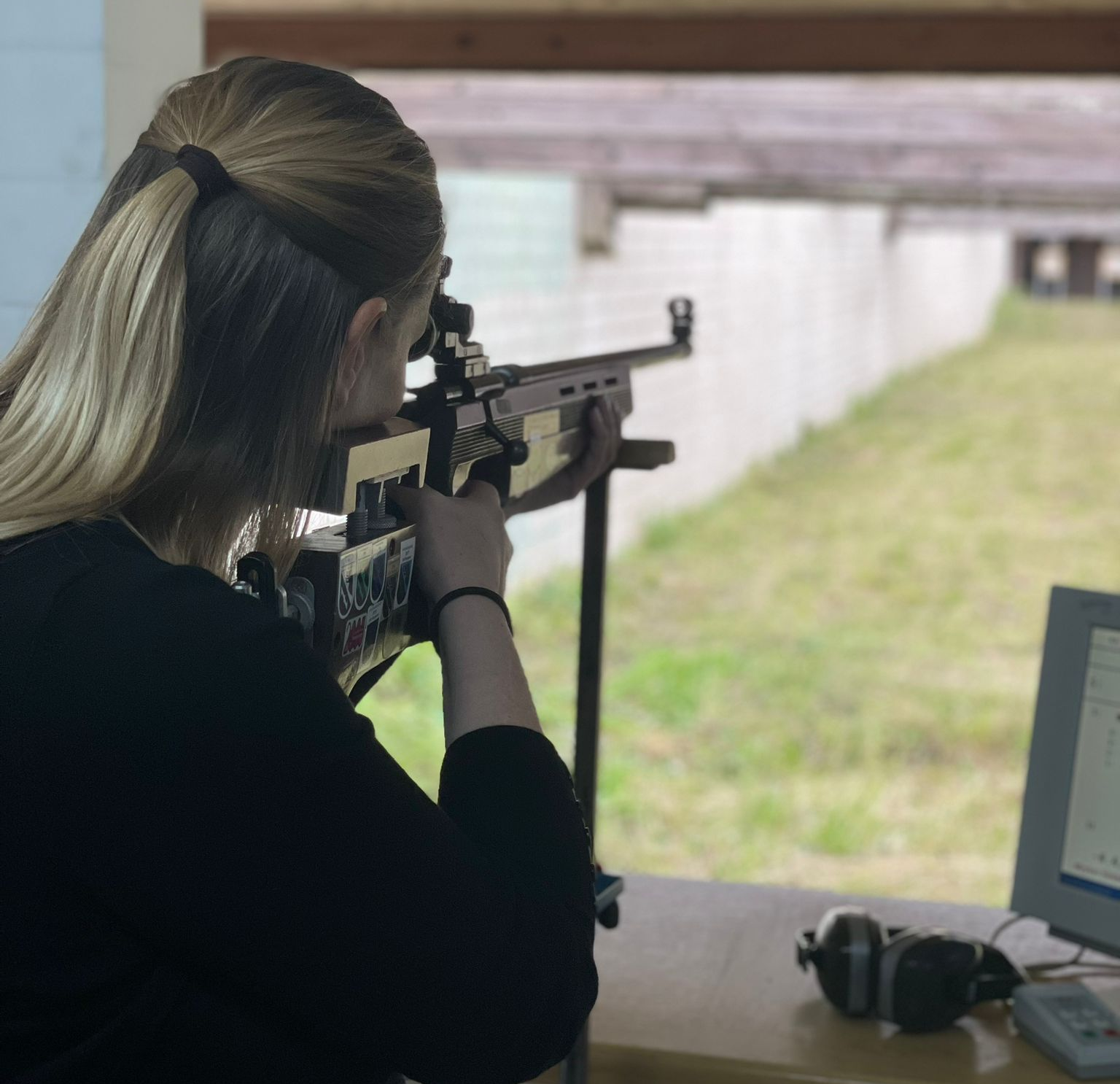 Eine Person zielt mit einem Gewehr auf einem Indoor-Schießstand, von hinten gesehen.