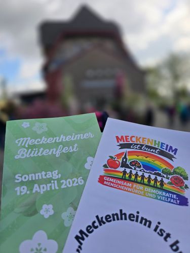 Zwei Flyer für das Meckenheimer Festival vor einem verschwommenen Gebäude im Freien
